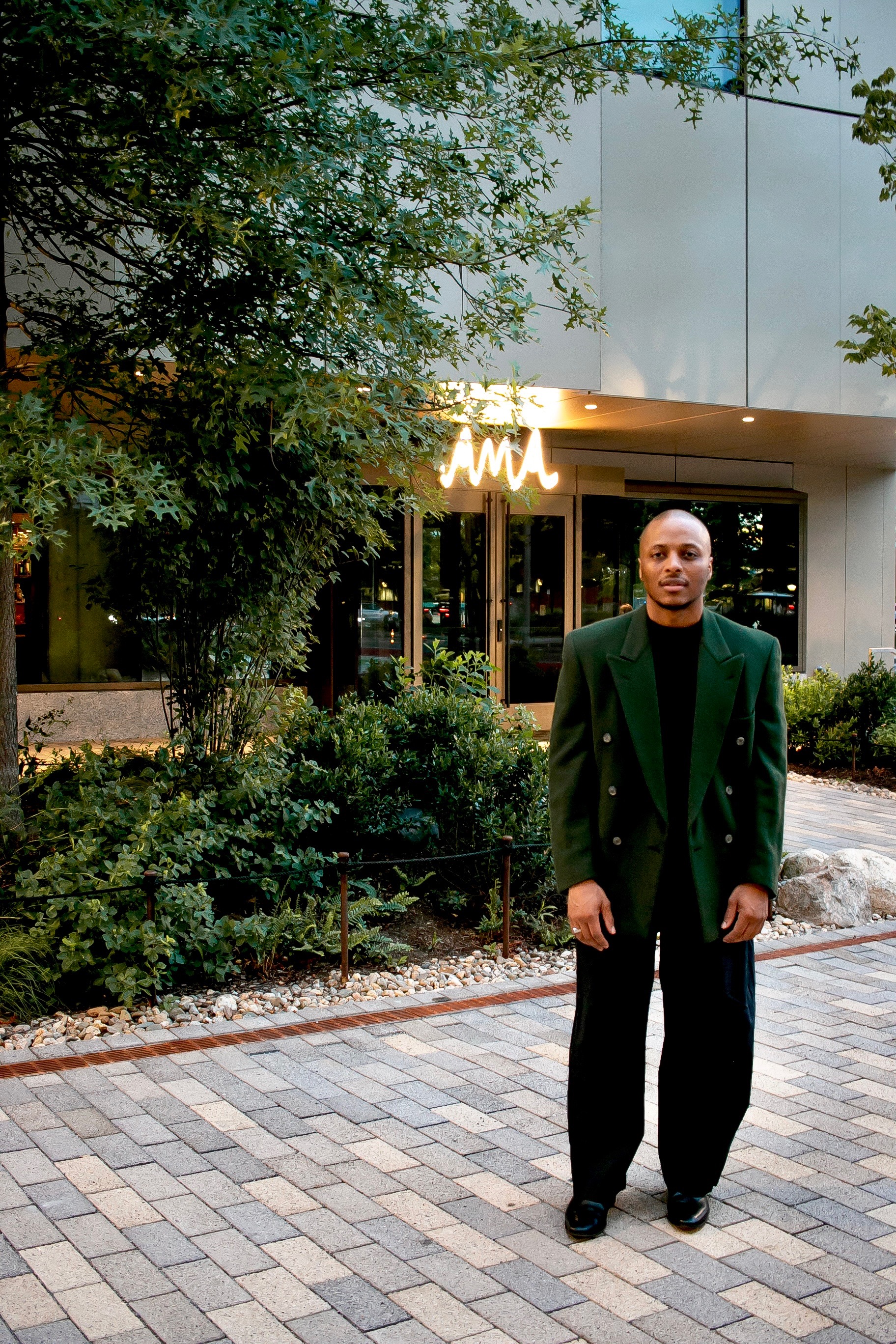 A man in a deep green blazer standing in front of AMA at The Atlas Hotel in Allston, Boston