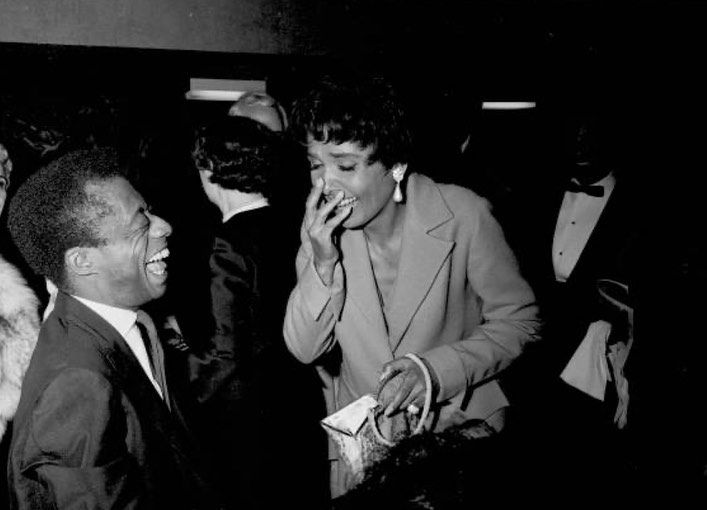 Black and white photograph of Jimmy Baldwin and Lena Horne laughing together at a social gathering