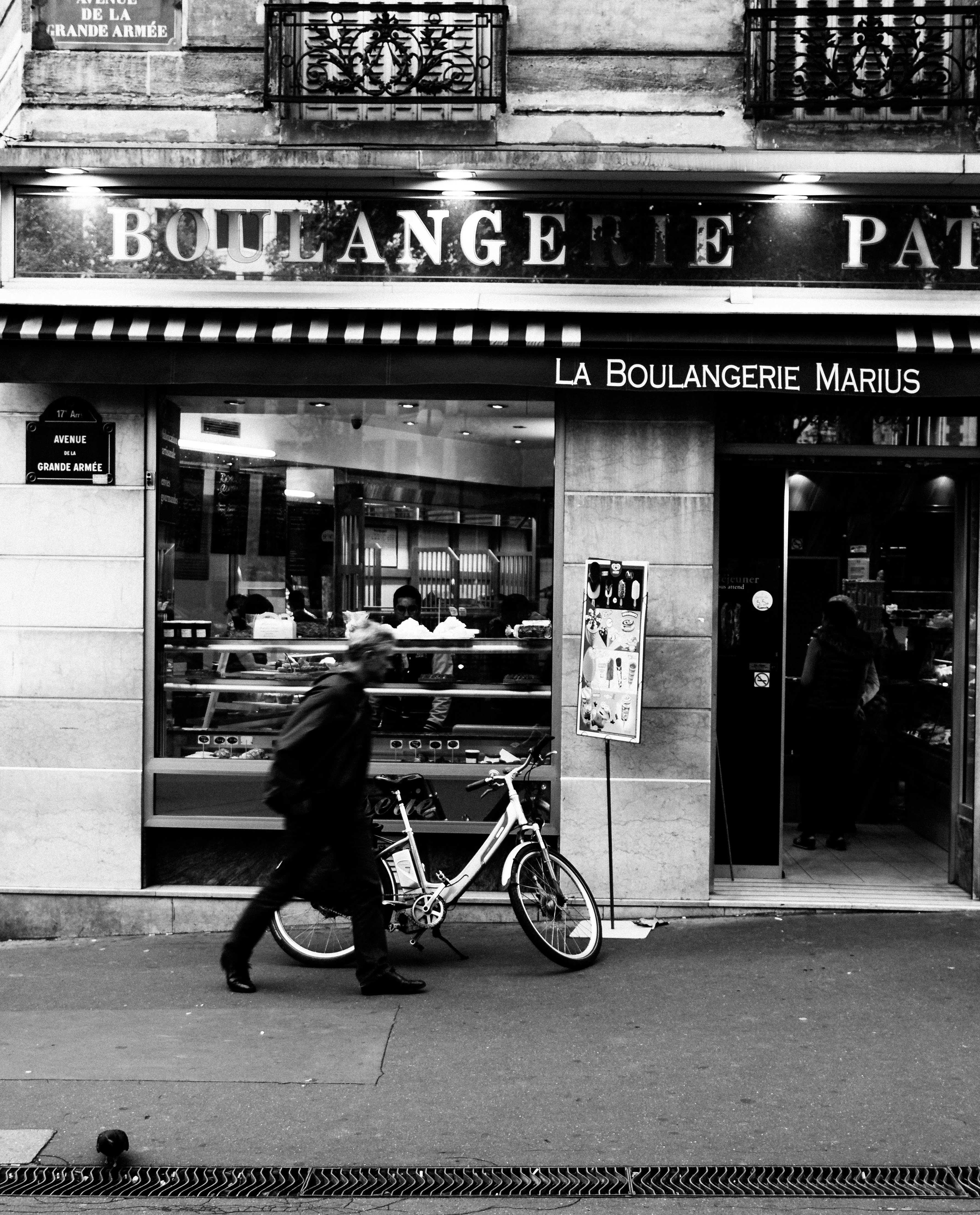 La Boulangerie - Black and white street photography of Parisian bakery with bicycle and walking figure