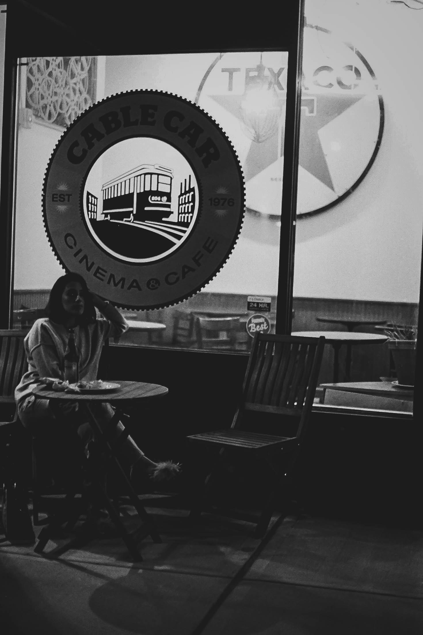 Michelle at Cable Car Cinema - Black and white photograph of woman sitting at table inside the historic Cable Car Cinema & Cafe with iconic logo visible on window