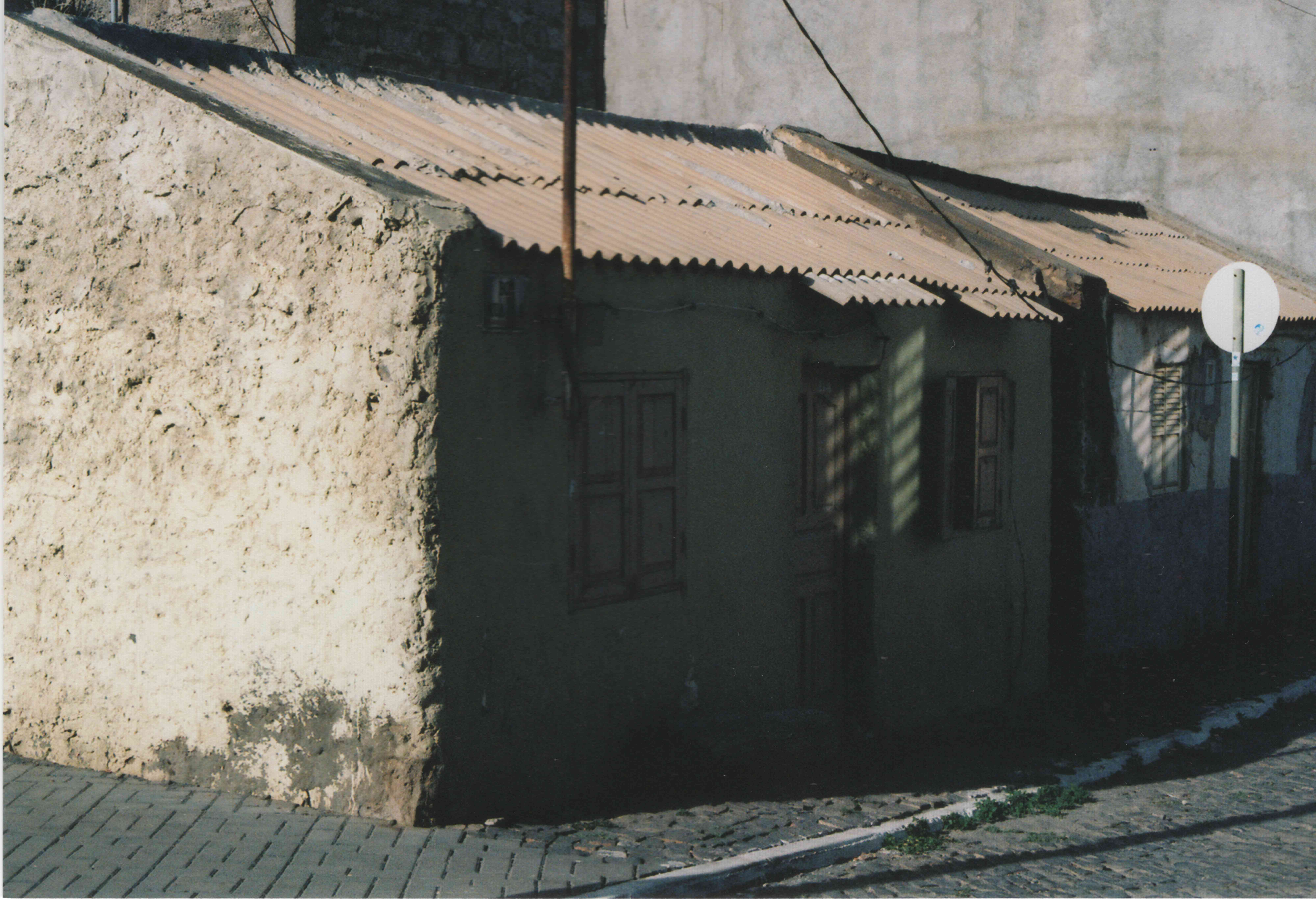 Traditional Cape Verdean building with weathered walls, corrugated metal roof, green doors and shutters on cobblestone street